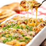 Portrait image of gnocchi alla Sorrentina served in a gratin dish being served with a spoon showing gooey mozzarella cheese strings featuring a title overlay