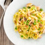 Portrait overhead image of salmon and pea pasta with tagliatelle pasta and crispy salmon skin and snipped chives