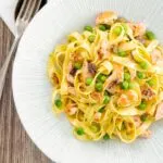 Portrait overhead image of salmon and pea pasta with tagliatelle pasta and crispy salmon skin and snipped chives