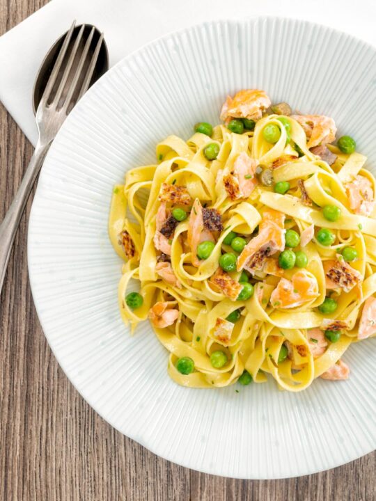 Portrait overhead image of salmon and pea pasta with tagliatelle pasta and crispy salmon skin and snipped chives