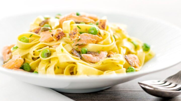 Landscape image of salmon and pea pasta with tagliatelle pasta and crispy salmon skin and snipped chives