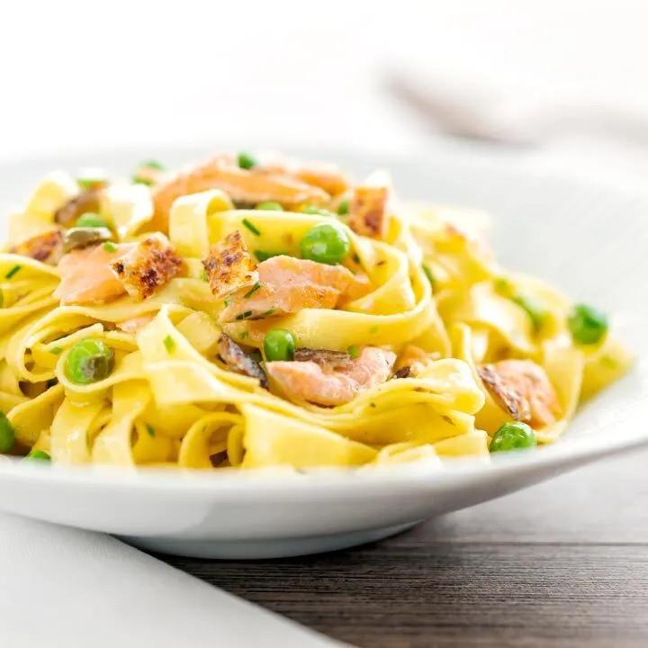 Square image of salmon and pea pasta with tagliatelle pasta and crispy salmon skin and snipped chives