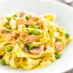Portrait image of salmon and pea pasta with tagliatelle pasta and crispy salmon skin and snipped chives