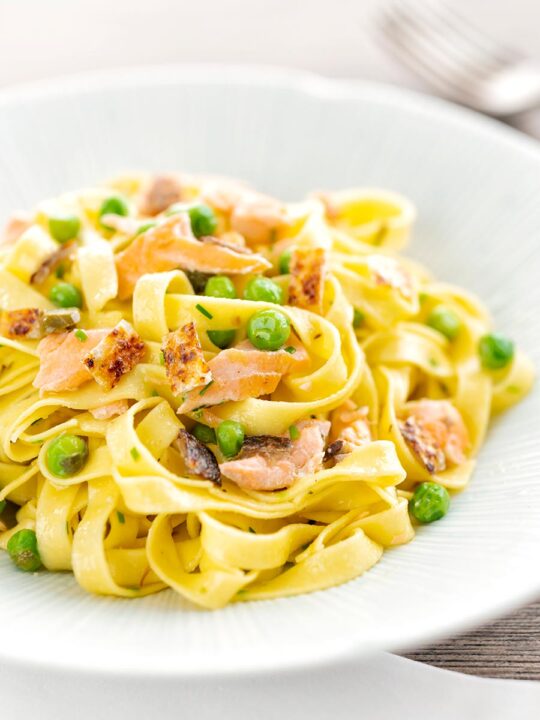 Portrait image of salmon and pea pasta with tagliatelle pasta and crispy salmon skin and snipped chives