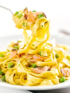 Portrait image of salmon and pea pasta with tagliatelle pasta and crispy salmon skin and snipped chives being picked up with a fork