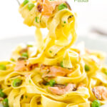 Portrait image of salmon and pea pasta with tagliatelle pasta and crispy salmon skin and snipped chives being picked up with a fork featuring a title overlay