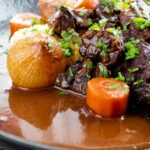 Portrait close up image of a slow cooker beef daube featuring carrots and whole small onions garnished with parsley