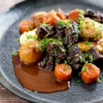 Portrait image of a slow cooker beef daube featuring carrots and whole small onions served with mashed potato and garnished with parsley