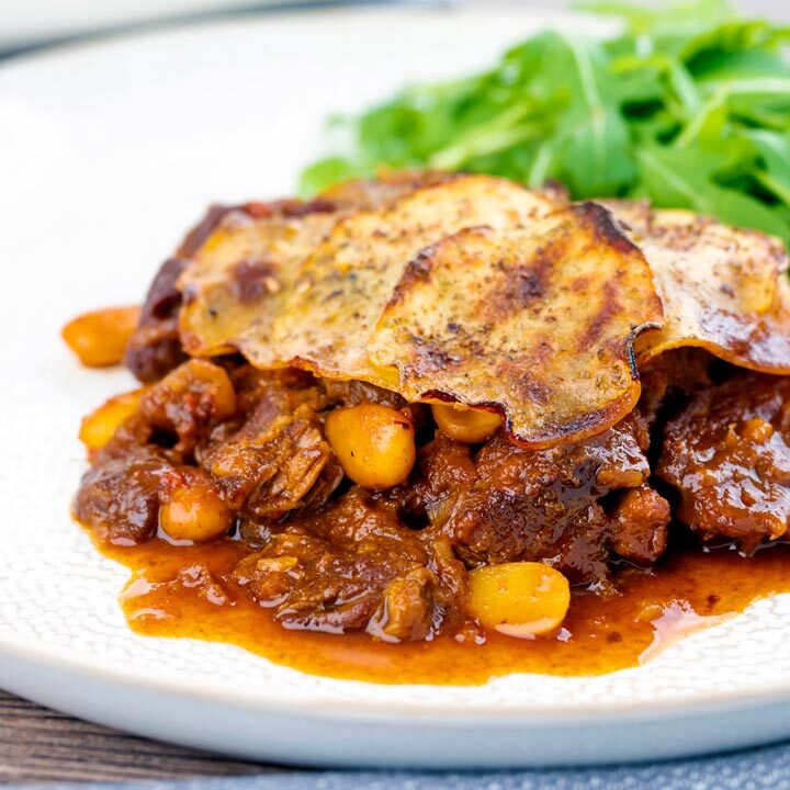 Square image of a sliced potato topped spicy beef hotpot with dried almonds and apricots