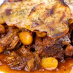 Portrait close up image of a sliced potato topped spicy beef hotpot with dried almonds and apricots
