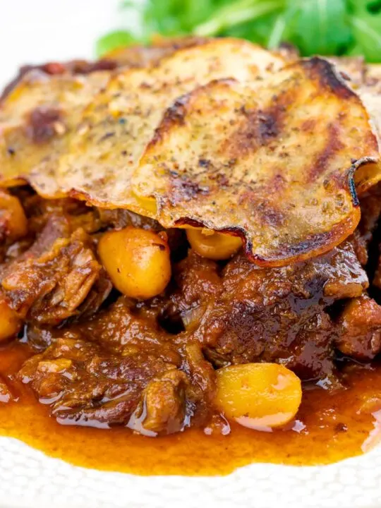 Portrait close up image of a sliced potato topped spicy beef hotpot with dried almonds and apricots