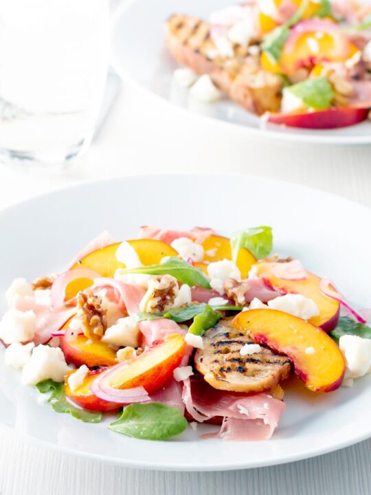 Two plates of pickled peach and goat cheese salad with Parma ham and chopped walnuts.