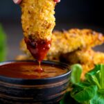 Crispy chicken goujons with one being dipped into a spicy dipping sauce