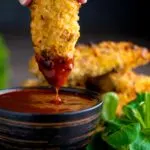 Crispy chicken goujons with one being dipped into a spicy dipping sauce
