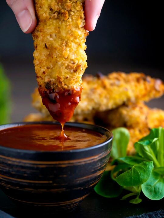 Crispy chicken goujons with one being dipped into a spicy dipping sauce