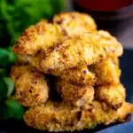 A pile chicken goujons in a hazelnut and breadcrumb with a spicy dipping sauce in the background