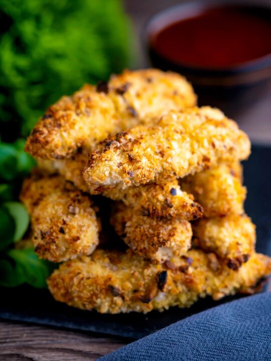 A pile chicken goujons in a hazelnut and breadcrumb with a spicy dipping sauce in the background