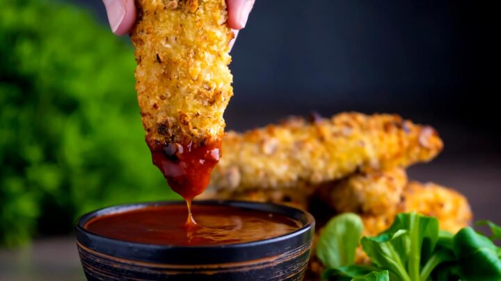 Crispy chicken goujons in a hazelnut and breadcrumb coating being dipped into a spicy dipping sauce