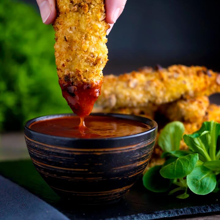 Close up chicken goujons in a hazelnut and breadcrumb coating being dipped into a spicy dipping sauce