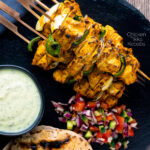 Overhead chicken tikka kebabs served with chapati, kachumber salad & raita featuring a title overlay