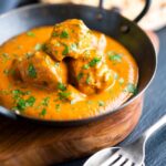Creamy chicken tikka masala in an iron karai with chapati in the background