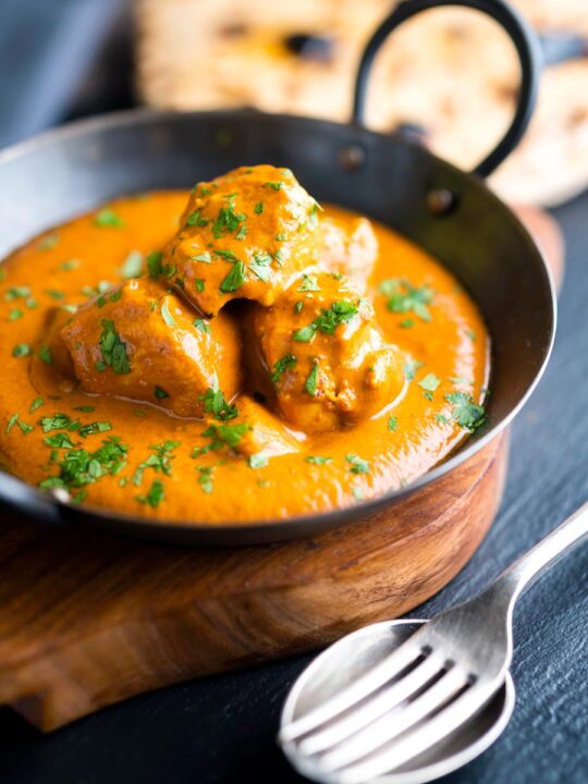 Creamy chicken tikka masala in an iron karai with chapati in the background