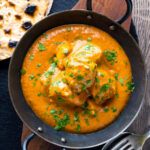 Creamy rich chicken tikka masala curry in an iron karai served with chapati featuring a title overlay