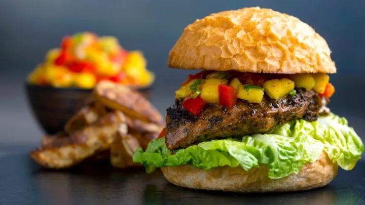 Jamaican jerk chicken burger with a mango salsa & potato wedges and a bowl of salsa