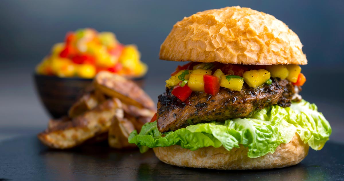 Jamaican jerk chicken burger with a mango salsa & potato wedges and a bowl of salsa