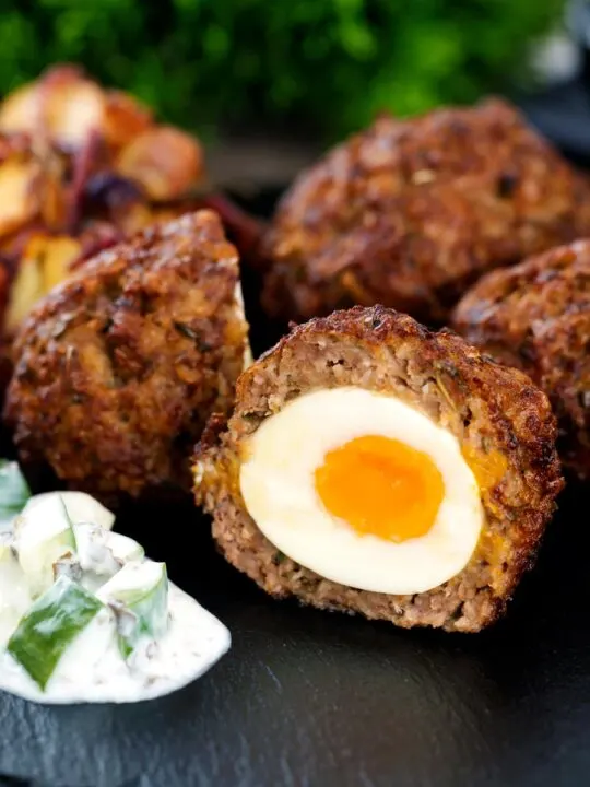 Nargis kebab or Indian Scotch eggs with one cut open to show jammy yolk served with cucumber raita