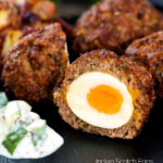 Nargis kebab or Indian Scotch eggs with one cut open to show jammy yolk served with cucumber raita featuring a title overlay