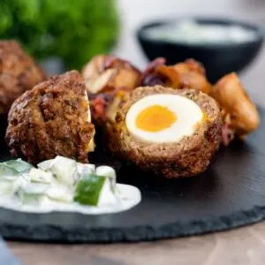 Nargis kebab or Indian Scotch eggs with one cut open to show jammy yolk served with cucumber raita
