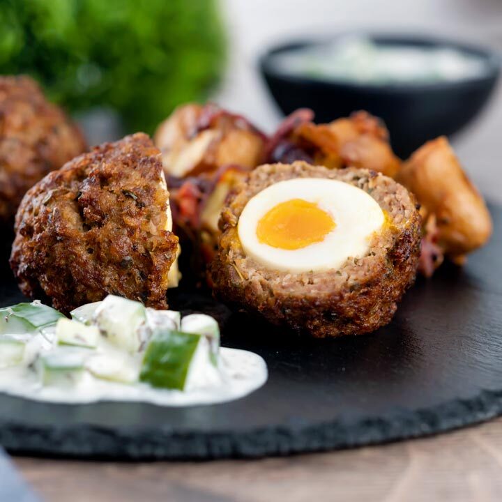 Nargis kebab or Indian Scotch eggs with one cut open to show jammy yolk served with cucumber raita