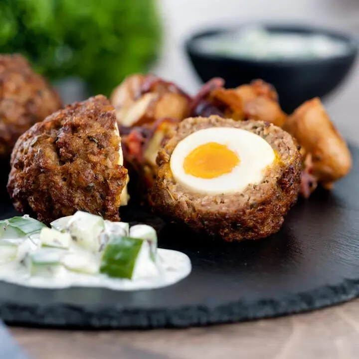 Nargis kebab or Indian Scotch eggs with one cut open to show jammy yolk served with cucumber raita