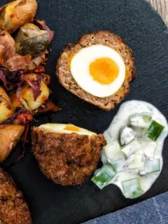 Overhead Nargis kebab or Indian Scotch eggs with one cut open to show jammy yolk served with cucumber raita