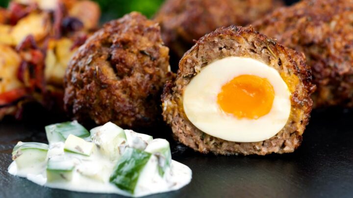 Close up Nargis kebab or Indian Scotch eggs with one cut open to show jammy yolk served with cucumber raita