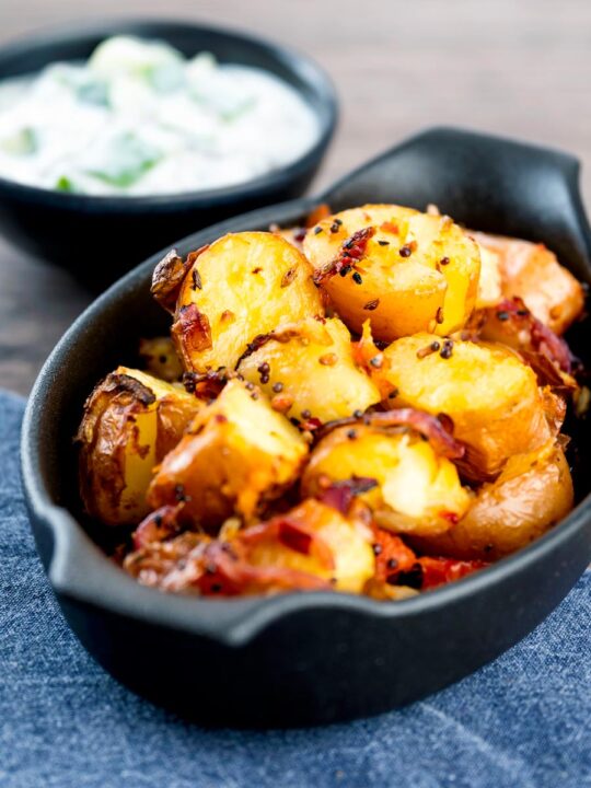 Roast Bombay potatoes or Bombay aloo in a black earthenware bowl served with raita