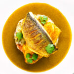 Overhead sea bass fillet curry served with fenugreek potatoes featuring a title overlay