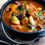 Hungarian bean goulash or babgulyas served in an iron bowl featuring a title overlay.