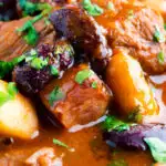 Close up Hungarian bean goulash or babgulyas served in an iron bowl featuring a title overlay.