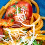 Tomato and bacon pasta close up garnished with parsley and pecorino cheese.
