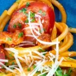 Tomato and bacon pasta close up garnished with parsley and pecorino cheese.