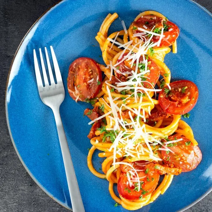 Overhead tomato and bacon pasta garnished with parsley and pecorino cheese on a blue plate.