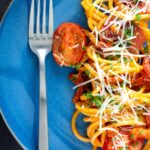 Overhead tomato and bacon pasta garnished with parsley and pecorino cheese served on a blue plate.