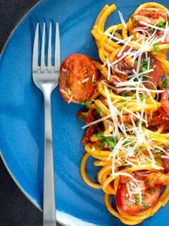 Overhead tomato and bacon pasta garnished with parsley and pecorino cheese served on a blue plate.