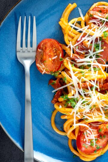 Overhead tomato and bacon pasta garnished with parsley and pecorino cheese served on a blue plate.
