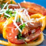 Close up tomato and bacon pasta garnished with pecorino cheese served on a blue plate.