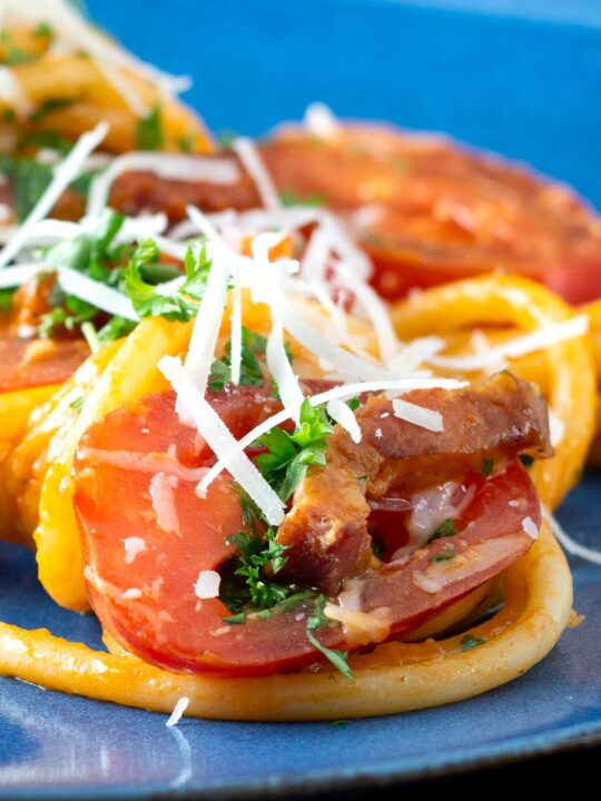 Close up tomato and bacon pasta garnished with pecorino cheese served on a blue plate.