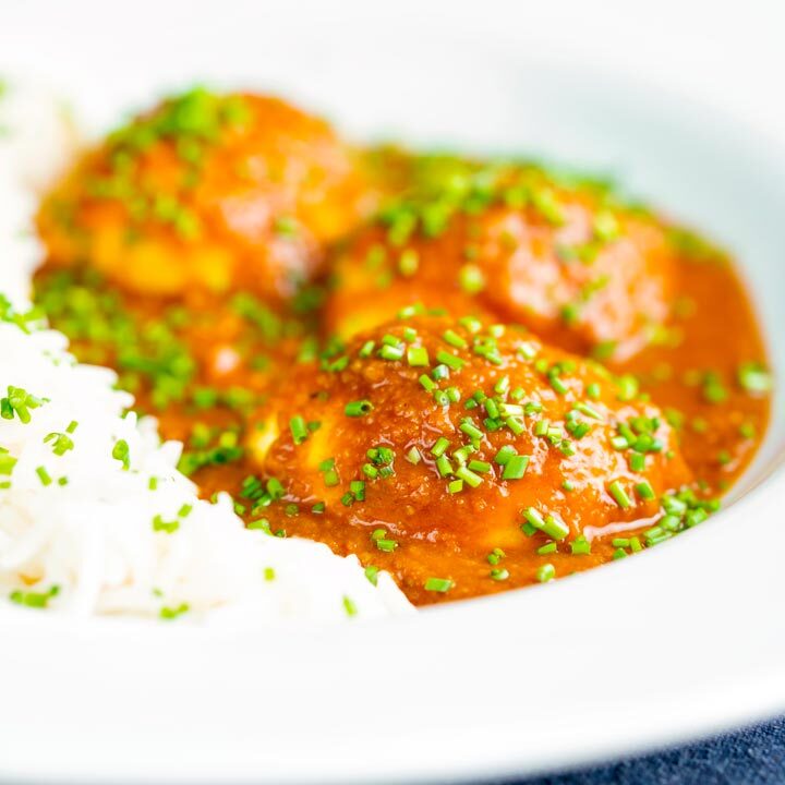 Egg curry or anda masala served with rice & snipped chives served in a white bowl.
