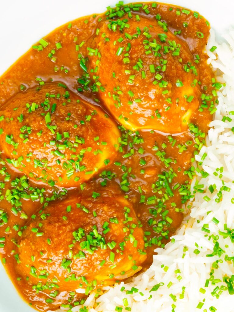 Close up egg curry or anda masala served with rice and snipped chives.